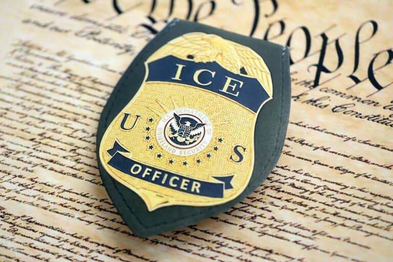 A U.S. ICE officer badge rests on a copy of the U.S. Constitution, with "We the People" visible in the background—a powerful image featured in Renee Good’s Law Q&A series.