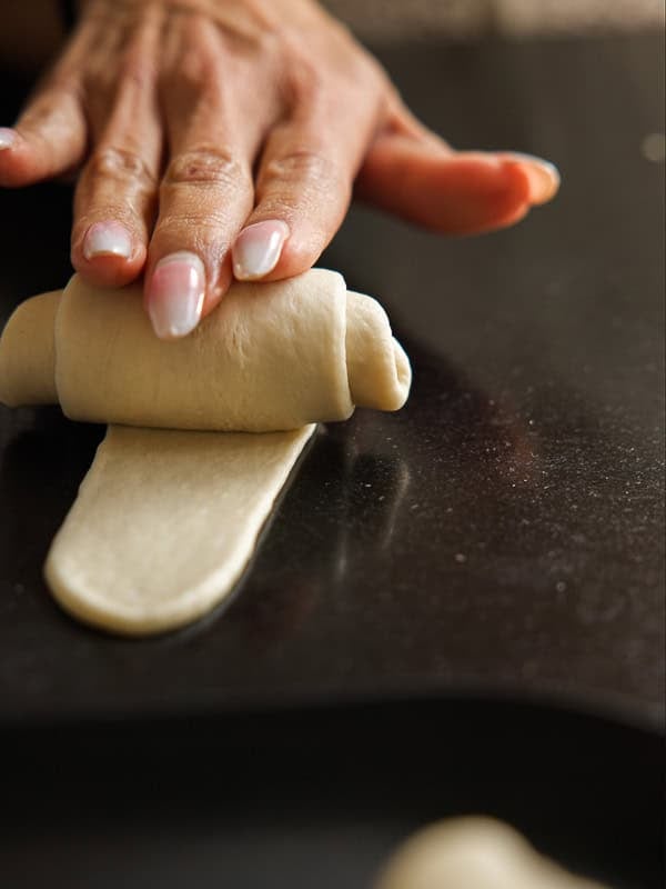 How to Make Viral Salt Bread Recipe (Easy and Vegan). 28 A close-up of a hand with manicured nails rolling a strip of dough on a dark surface, forming a pastry or bread roll—perfect for trying out that viral bread everyone's talking about.