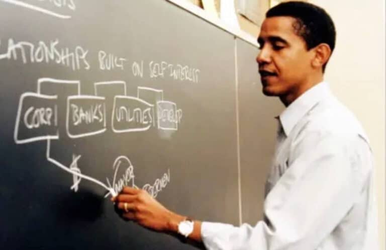 A man in a white shirt writes and draws diagrams with rectangles and text on a blackboard in a classroom setting, discussing topics like CORP, BANKS, UTILITIES, and RELATIONSHIPS BUILT ON SELF-INTEREST.