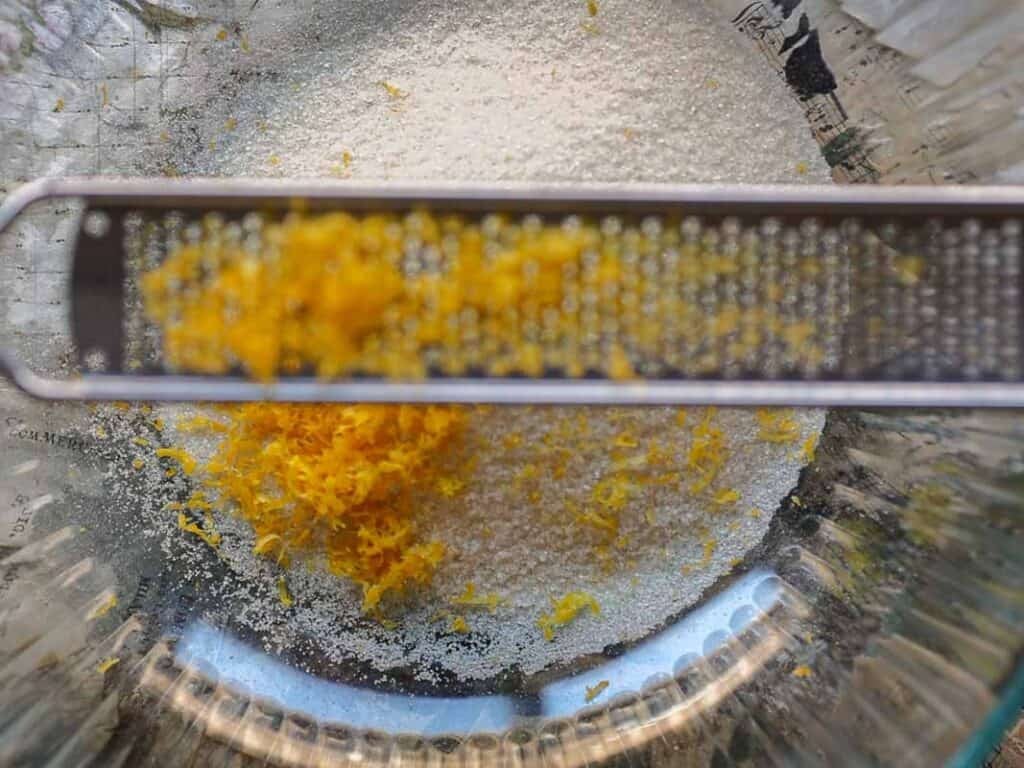 Delicious and Easy Vegan Lemon Poppyseed Muffins. 5 A close-up of a glass bowl with sugar and fresh lemon zest, with a metal zester resting across the bowlโperfect ingredients for vegan lemon poppyseed muffins.