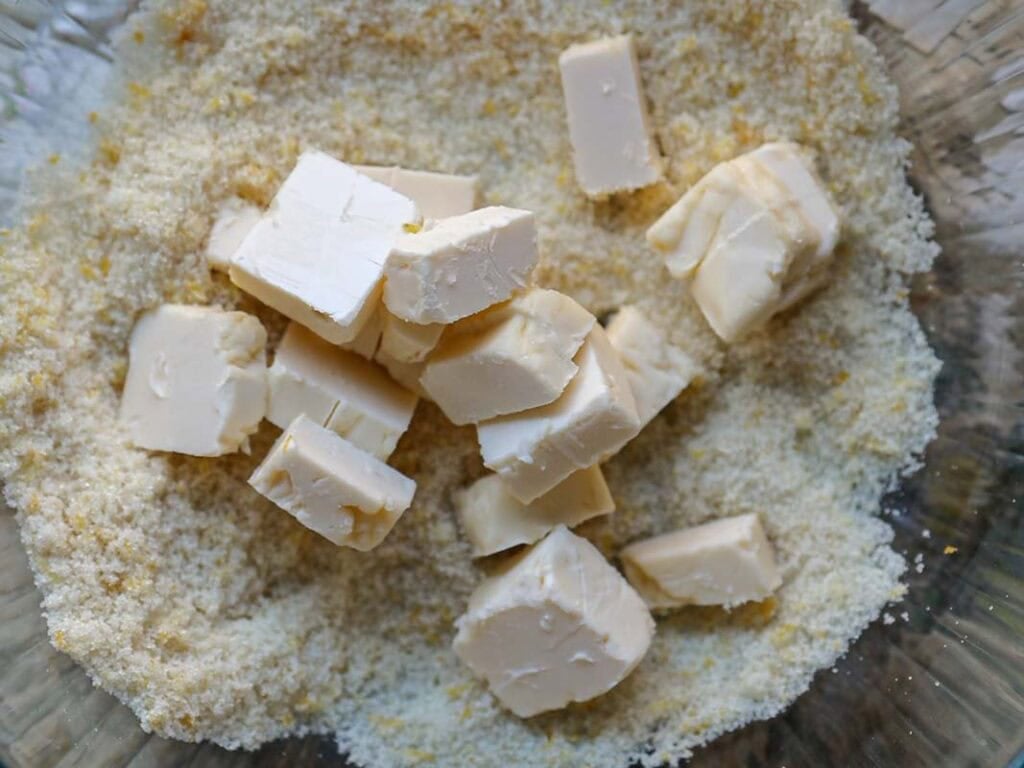 Delicious and Easy Vegan Lemon Poppyseed Muffins. 8 Cubes of butter sit atop a mixture of flour and possibly sugar in a clear glass bowl, ready to be mixed for baking delicious vegan lemon poppyseed muffins.