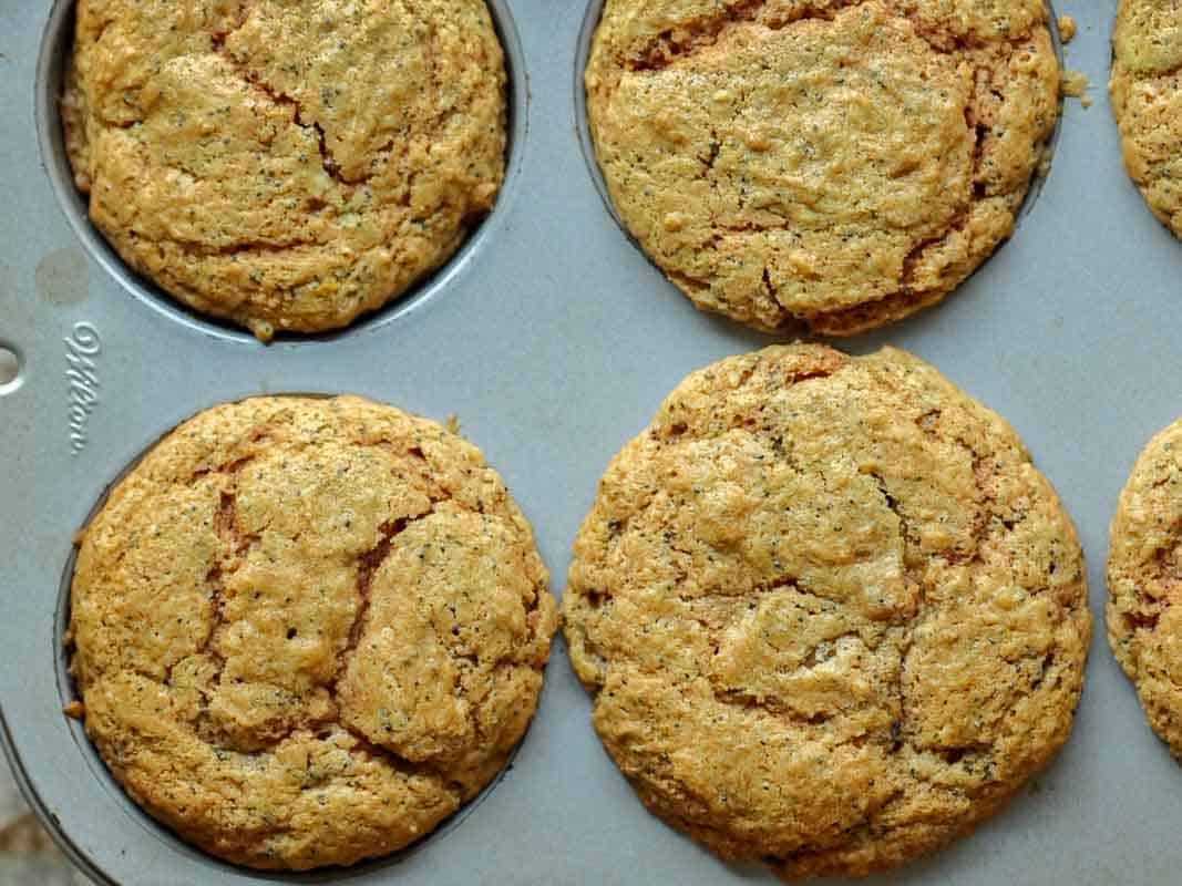 Delicious and Easy Vegan Lemon Poppyseed Muffins. 3 Close-up of a metal muffin tin holding six golden-brown, freshly baked vegan lemon poppyseed muffins with cracked tops.