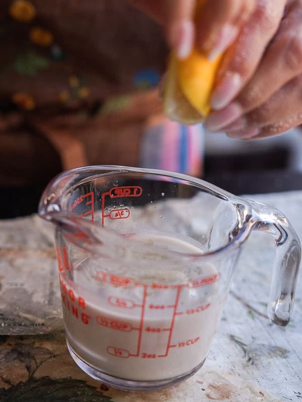 Delicious and Easy Vegan Lemon Poppyseed Muffins. 7 A hand squeezes a lemon half above a glass measuring cup of cloudy liquid, likely lemon juice mixing with milk or creamโperfect for preparing vegan lemon poppyseed muffins on a kitchen counter.