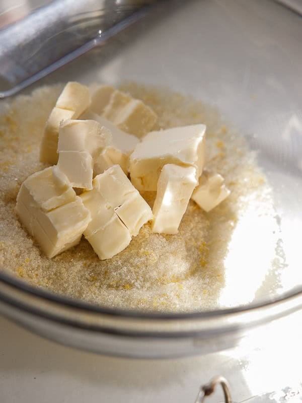 Easy Vegan Lemon Cookies Recipe (Soft and Lemony!) 9 Cubes of butter on top of a mound of granulated sugar in a clear glass mixing bowl, ready to be mixed for delicious lemon cookies.