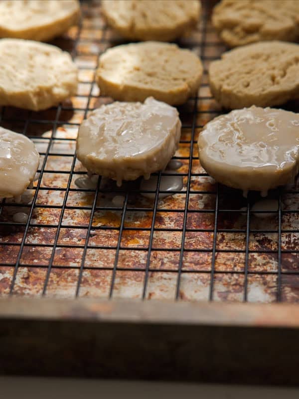 Easy Vegan Lemon Cookies Recipe (Soft and Lemony!) 29 Round lemon cookies cooling on a wire rack, with some cookies covered in a shiny glaze and others plain. The rack is set over a baking sheet that has drips of glaze on it.