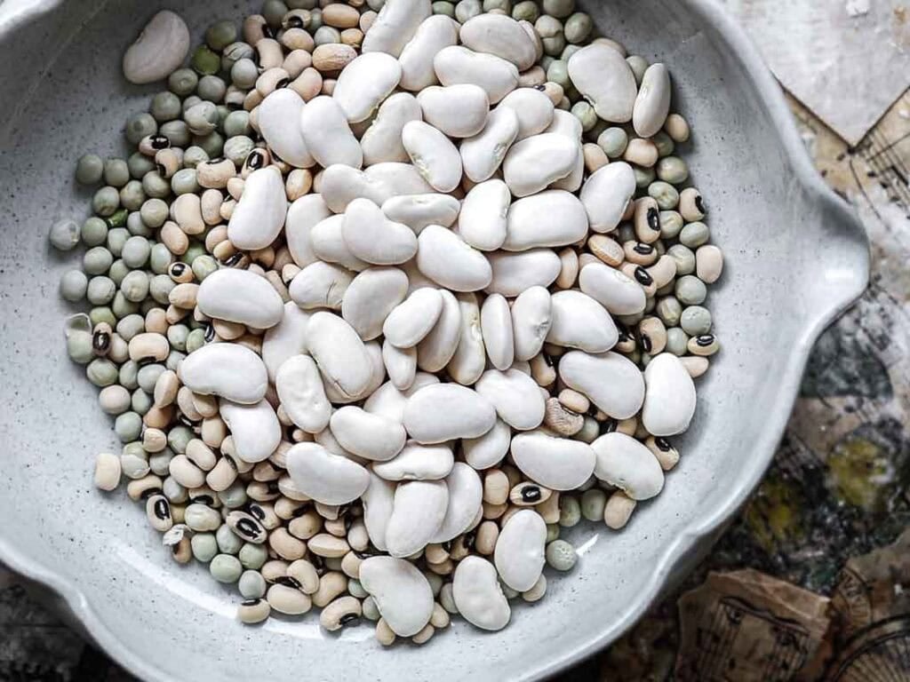 Gut Healthy Korean Multigrain Rice - Japgokbap (잡곡밥) 5 A white ceramic bowl filled with a variety of dry beans and peas, like those used in Japgokbap, Korean multigrain rice, known for being gut healthy. The bowl is set on a textured surface with scattered papers.
