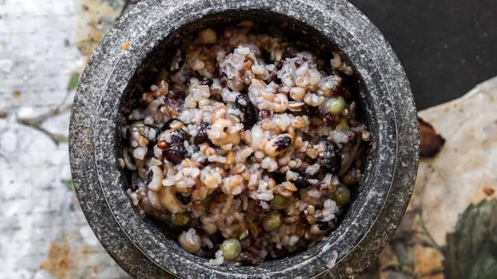 A close-up of a rustic stone bowl filled with gut healthy Korean multigrain rice, or Japgokbap, featuring an array of grains, beans, and seeds in earthy shades of brown, black, and green.