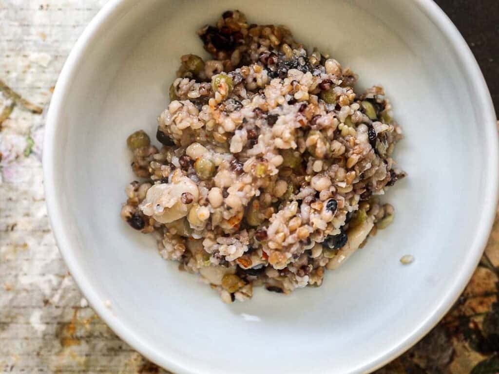 Gut Healthy Korean Multigrain Rice - Japgokbap (잡곡밥) 3 A close-up of a white bowl filled with gut healthy Korean multigrain rice, or japgokbap, featuring quinoa, lentils, and seeds on a rustic wooden surface.