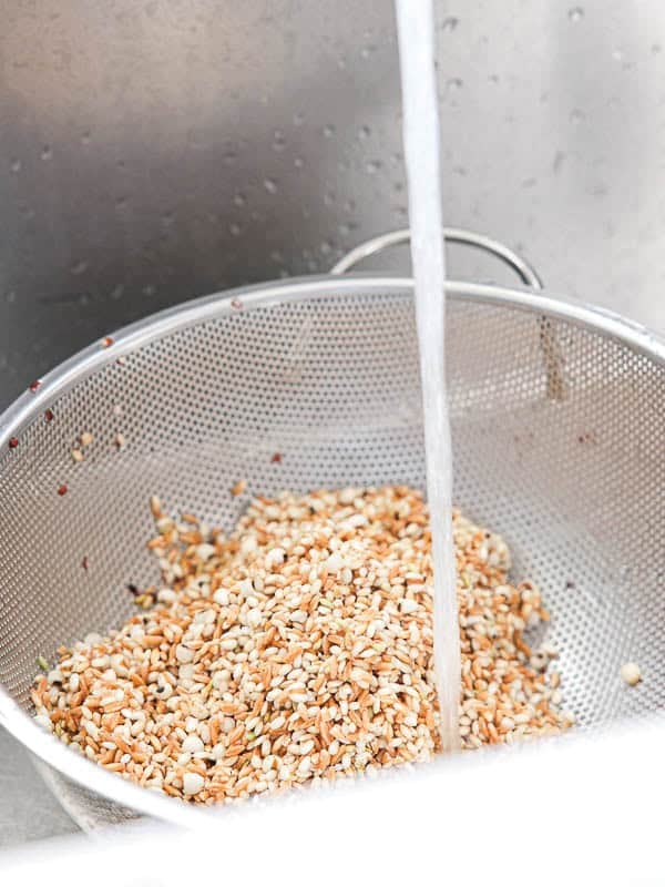 Gut Healthy Korean Multigrain Rice - Japgokbap (잡곡밥) 14 A metal colander filled with Korean multigrain rice, or Japgokbap, is placed in a sink under running water, being rinsed for a gut healthy meal.