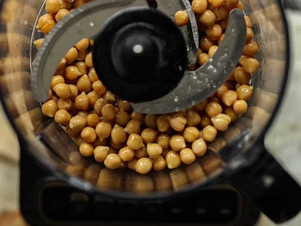 Easy & Delicious Hi-Protein Chickpea Cutlets 4 Overhead view of chickpeas inside a food processor with metal blades, ready to be blended for homemade chickpea cutlets.