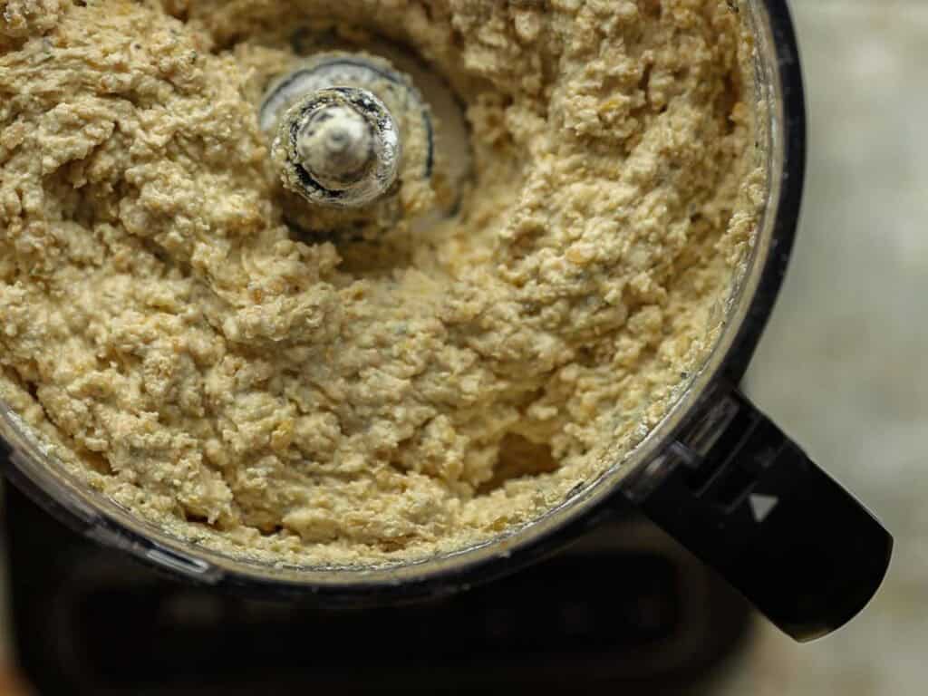 Easy & Delicious Hi-Protein Chickpea Cutlets 6 Close-up view of a food processor filled with a thick, beige mixture for chickpea cutlets, with textured swirls around the central blade, suggesting a well-blended batter or dough.