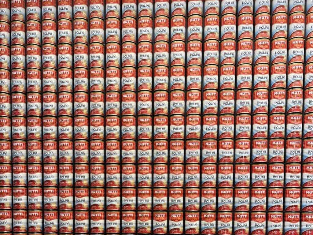 Da Vinci & Mutti: A Visit to Parma, Italy. 10 Rows of Mutti Polpa finely chopped tomatoes cans are stacked tightly against each other, creating a colorful, repetitive pattern with red, white, and yellow labels—true to the rich tomato tradition of Parma, Italy.