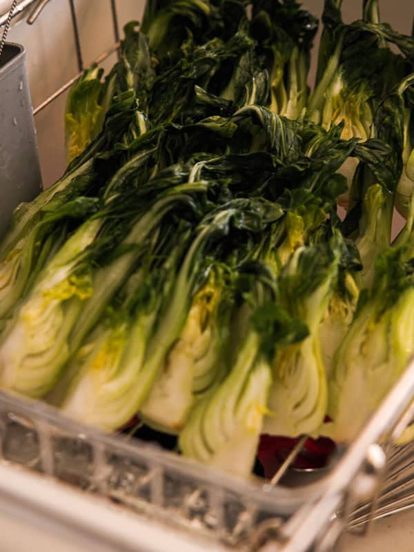 BEST Baby Bok Choy Kimchi Recipe - Easy & Delicious 37 Several halved heads of fresh leafy green vegetables, possibly escarole or romaine lettuce—and perhaps even some bok choy kimchi—are arranged in rows inside a metal tray or rack, ready for washing or drying.