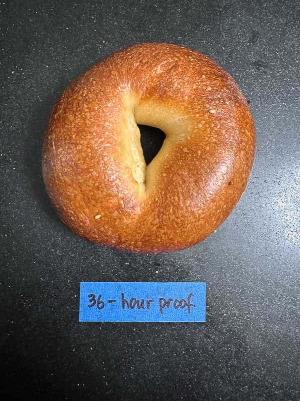 How to Make Delicious NY Style Bagels - Step by Step Guide. 82 A golden-brown NY style bagel rests on a dark surface, with a blue label below it that reads 36-hour proof.