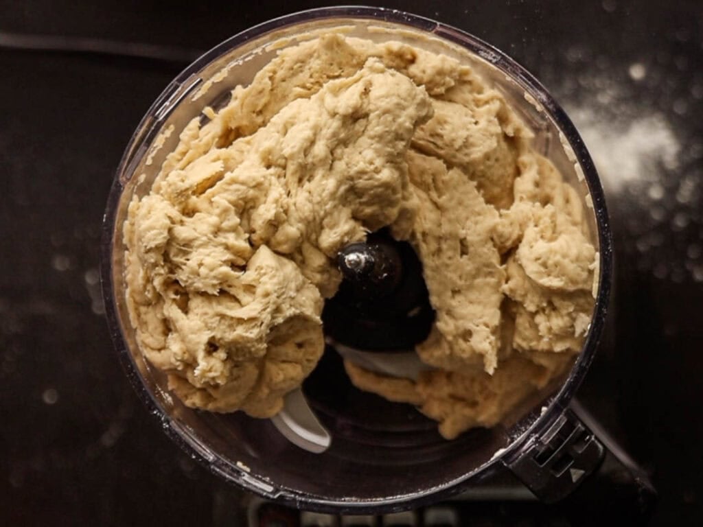 How to Make Delicious NY Style Bagels - Step by Step Guide. 21 A food processor bowl filled with freshly mixed dough for NY style bagels, shown from above on a dark surface with some flour scattered nearby.