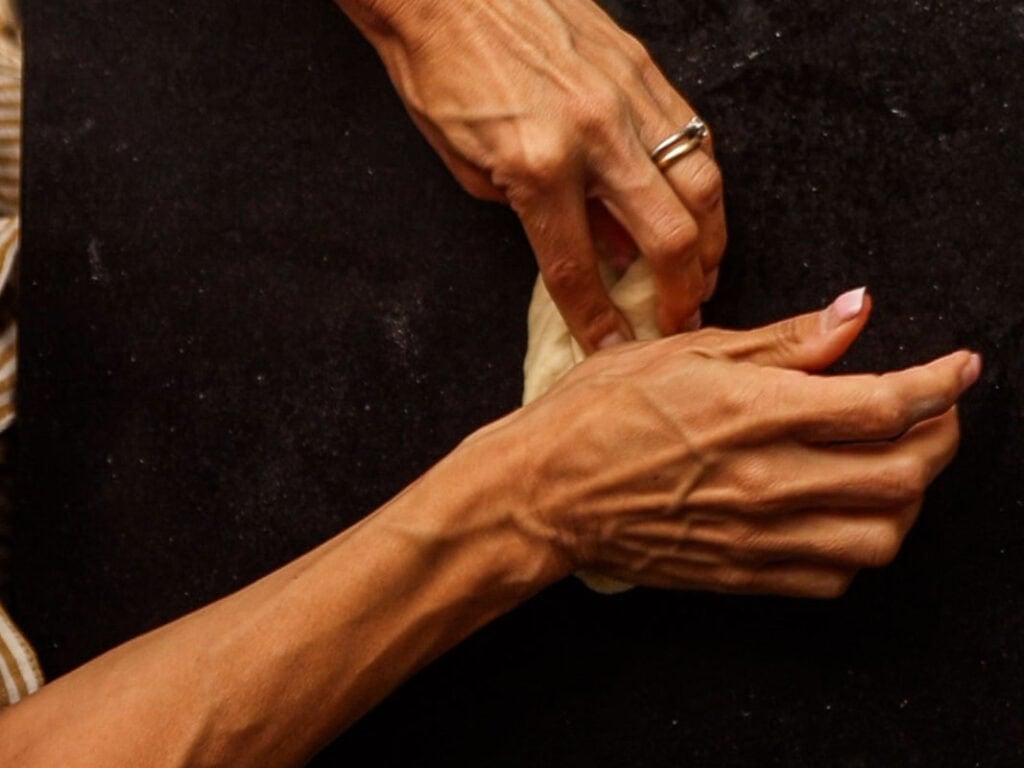 How to Make Delicious NY Style Bagels - Step by Step Guide. 27 A close-up of two hands kneading dough on a dark surface, with one hand wearing a ring—perfectly capturing the artistry behind making classic NY style bagels.