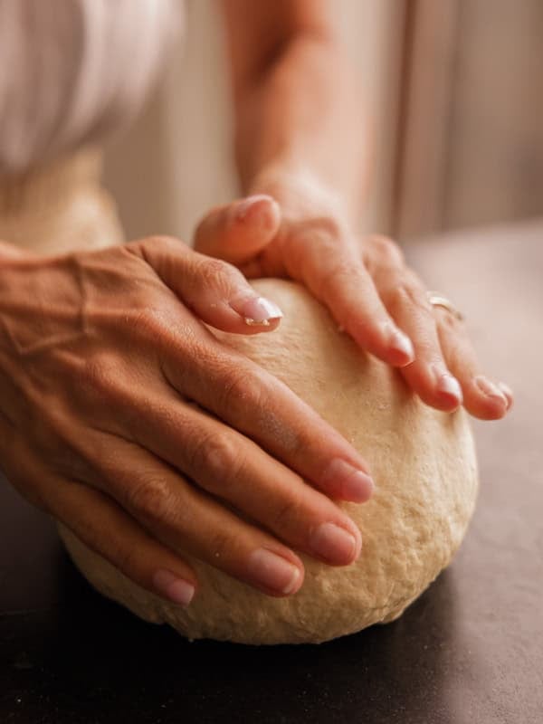 How My Bagels Triggered The Sexist In Me. 2 Close-up of hands kneading a ball of dough on a dark surface, with natural light coming from a window in the background—perfect for shaping authentic NY style bagels.