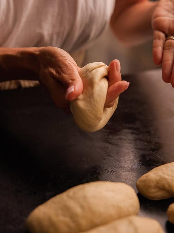 How to Make Delicious NY Style Bagels - Step by Step Guide. 42 A person shapes raw bread dough on a dark surface with several dough pieces nearby, preparing them by hand in the traditional fashion of NY style bagels.