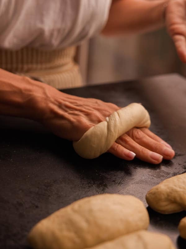 How to Make Delicious NY Style Bagels - Step by Step Guide. 43 A person wraps dough around their fingers on a dark surface, preparing to shape it into classic NY style bagels, with several pieces of dough nearby.