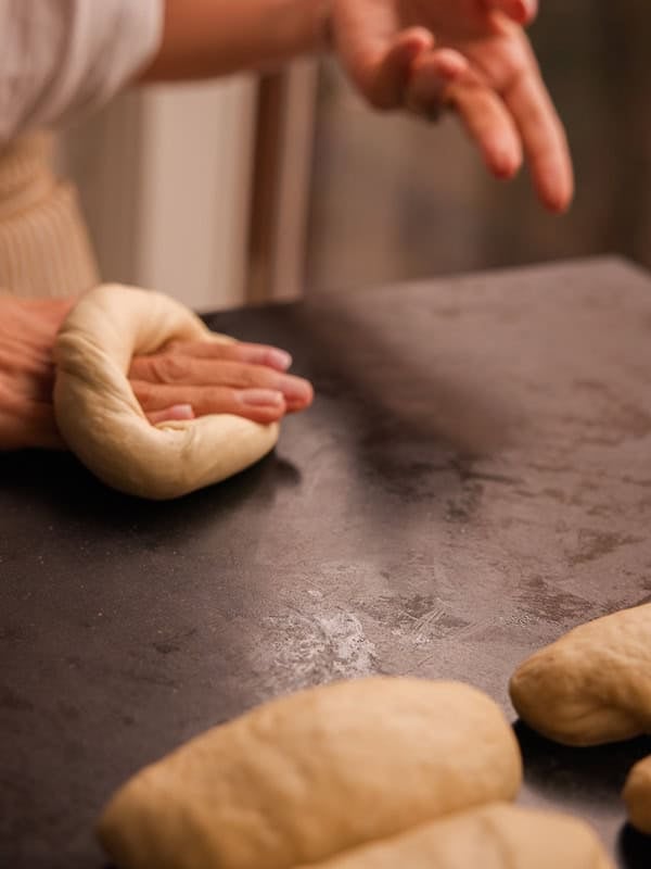 How to Make Delicious NY Style Bagels - Step by Step Guide. 46 A person shapes dough into a ring on a dark countertop, carefully preparing ny style bagels, with several pieces of dough resting nearby.