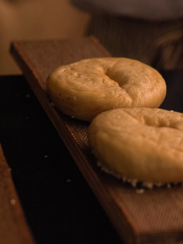 How to Make Delicious NY Style Bagels - Step by Step Guide. 68 Two plain NY style bagels with a light golden color rest on a wooden board. The lighting is warm and soft, highlighting the texture of the bagels.