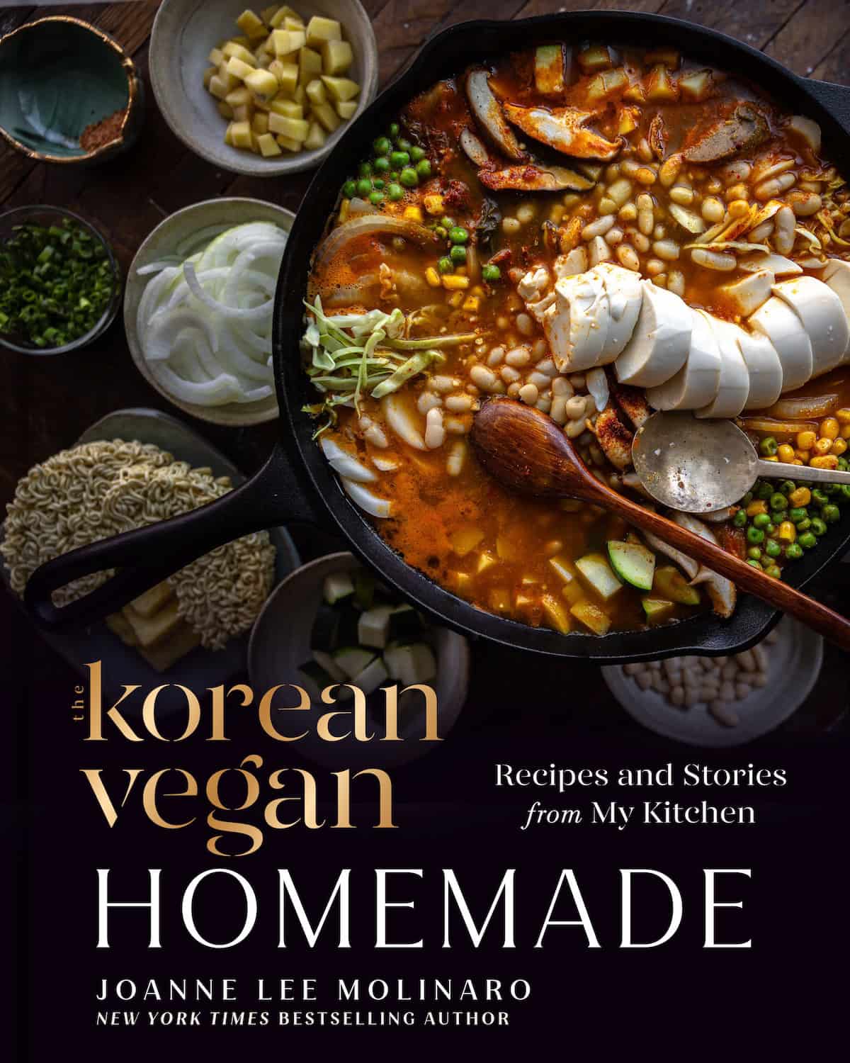 Home 18 A cookbook cover shows a skillet of Korean Vegan stew with tofu, beans, and vegetables, surrounded by bowls of ingredients. The title reads The Korean Vegan Cookbook by Joanne Lee Molinaro.